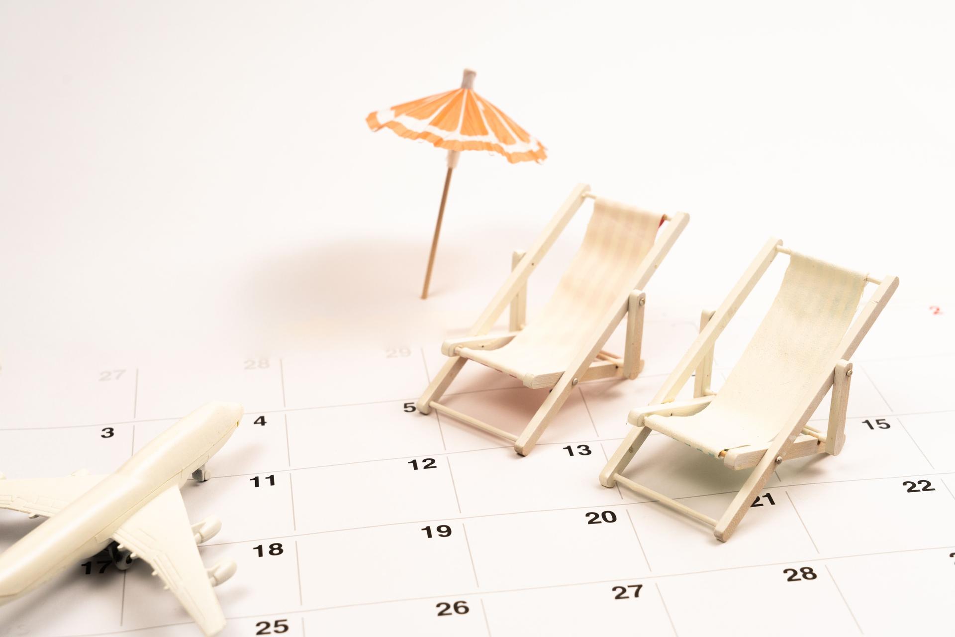 Miniature airplane, deck chairs and parasol sit on a calendar, symbolizing vacation planning and booking